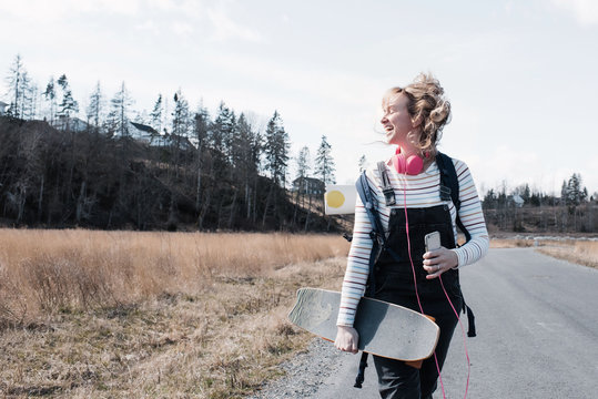 woman joyfully walking along with her skateboard and yoga mat singing