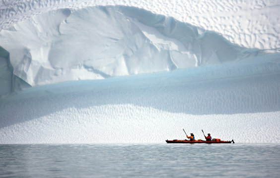 two men rowing their sea kayak along an iceberg in Greenland