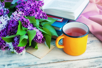 Bouquet of a lilac, a yellow сup and books оn wooden background, selective focus.