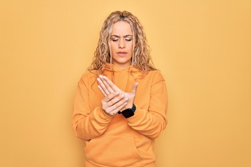 Young beautiful blonde sporty woman wearing casual sweatshirt over yellow background Suffering pain on hands and fingers, arthritis inflammation