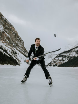 man in suit and ice skates juggles hockey puck on frozen Lake Louise