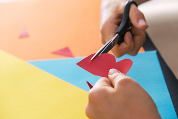 Paper crafts for kids. Child hands cutting colored paper with scissors at the table
