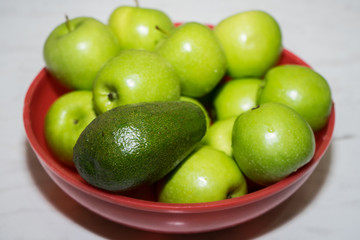 green apples and avocado in a red cup on the table