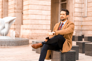 An elegant man sitting next to a fountain