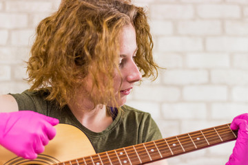A young pretty teen girl stares at the camera and plays the guitar in rubber gloves, learning...