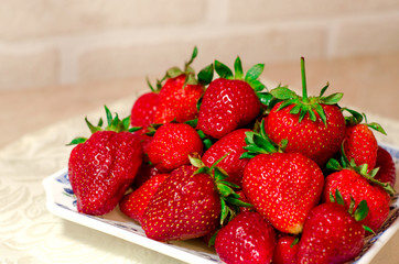 A plate with ripe red fresh strawberries in close-up against a white brick wall.