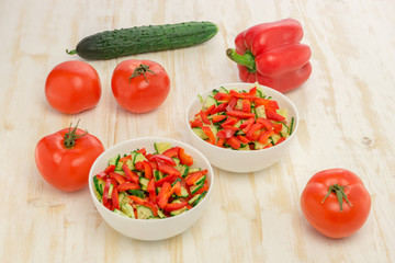 Fresh salad of sliced green cucumbers, red tomatoes and bell peppers on wood table. Vegetables. Gluten-free, lactose-free vegan food