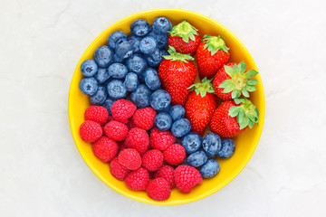 Berries in a yellow bowl on a light background, raspberries, strawberries, blueberries, top view
