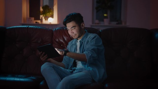 Happy and Positive Asian guy win played in game on tablet at home on sofa.
