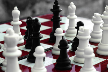 White and black chess in a chaotic arrangement, on a red-white chessboard on a stone background