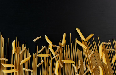 yellow raw homemade spaghetti and penne pasta on a black concrete background at the bottom of the frame. Top view. The concept of cooking and diet. Copy space