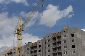 Fototapeta na wymiar Construction site. Construction site with a crane. A concrete gray building under construction against a blue sky and clouds.