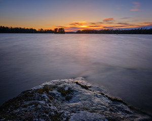 cliff goes out into the still lake with forest and sunset in the background