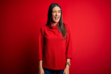 Fototapeta premium Young beautiful brunette woman wearing casual sweater over isolated red background winking looking at the camera with sexy expression, cheerful and happy face.