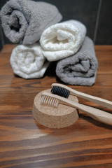 Obraz na płótnie Canvas Where are the bamboo toothbrushes lying on a cork on a wooden table in the background Three small towels of white and gray