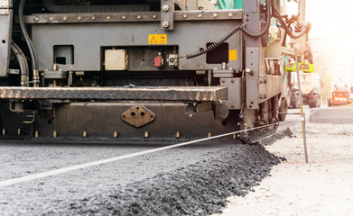 Paver machine is laying fresh asphalt on city road