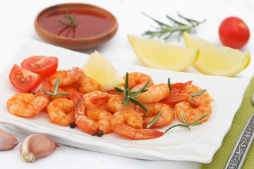 Delicious sauteed shrimps with sauce and lemon on white plate. Grilled tiger shrimps with rosemary and lspices.