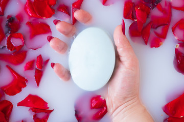 Female hand hold soap against the background of milk or white water with rose petals