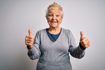 Senior beautiful grey-haired woman wearing golden queen crown over white background approving doing positive gesture with hand, thumbs up smiling and happy for success. Winner gesture.