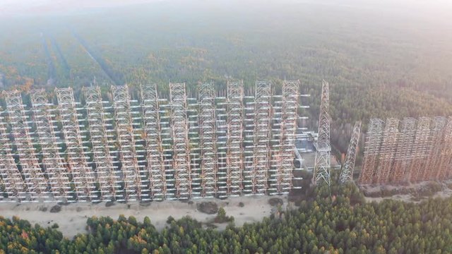 Drone flight over duga 3 radar antenna in the Chernobyl exclusion zone. Secret missile military area with sunset sun and surrounded by forest	