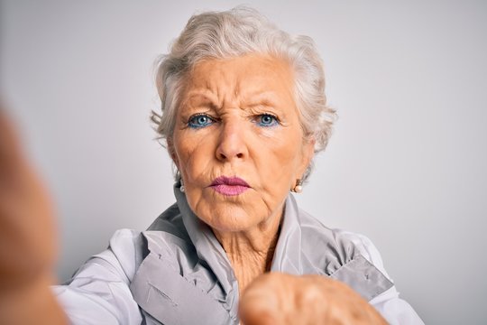 Senior beautiful grey-haired woman making selfie by camera over isolated white background pointing with finger to the camera and to you, hand sign, positive and confident gesture from the front