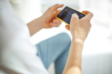 A young man with a phone in his hands is playing. A teenager plays on the phone at home.