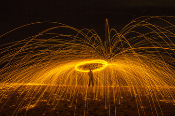 Long exposure silhouette of unrecognizable person spinning burning stick emitting sparkles while dancing with fire at night