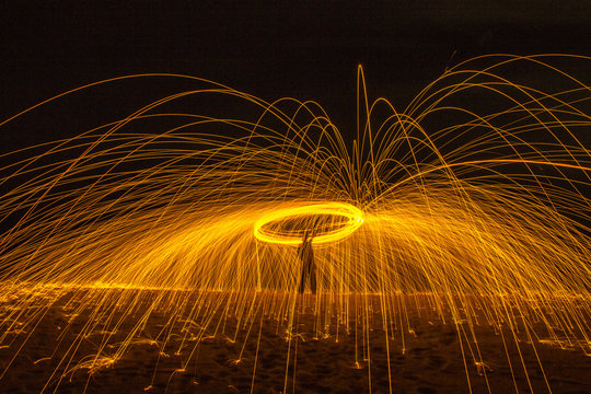 Long exposure silhouette of unrecognizable person spinning burning stick emitting sparkles while dancing with fire at night