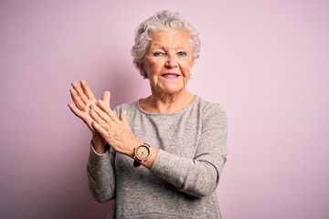 Senior beautiful woman wearing casual t-shirt standing over isolated pink background clapping and...