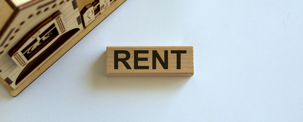 Wooden block form the word 'rent' near miniature house. Beautiful white background, copy space.