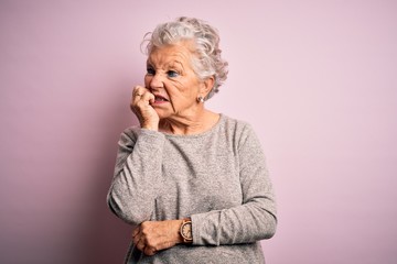 Senior beautiful woman wearing casual t-shirt standing over isolated pink background looking stressed and nervous with hands on mouth biting nails. Anxiety problem.