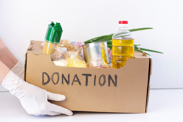 donation box. in hands in rubber gloves is a cardboard box with the inscription donation with food and protective masks and a disinfectant on a white background.