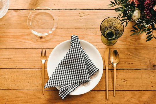 From above top view wooden table set for a meal with plate,cutlery, glass and napkin near beautiful bouquet of miscellaneous flowers with green plant twigs in vase