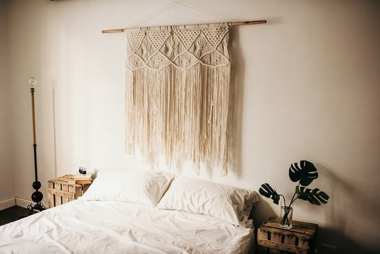Vintage macrame decoration hanging on wall over comfortable bed in cozy bedroom at home