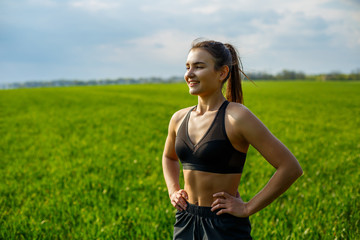 Naklejka na ściany i meble Girl athlete does warm-up outdoors, exercises for muscles. Young woman go in for sports, healthy lifestyle, athletic body. She is in sportswear, black top and shorts. Sport concept.
