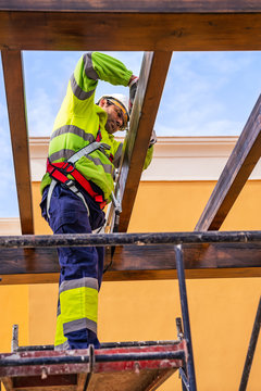 From below side view of male technician in work wear standing on scaffolding and preparing for installation of solar panel on wooden construction
