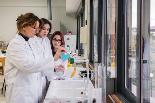 Female students watching mentor conducting experiment in lab
