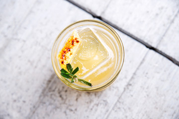 Fresh penicillin alcoholic cocktail with a slice of orange and ice cubes. An alcoholic Scottish penicillin cocktail with lemon, ginger sprig of rosemary and burnt sugar. light white gray background