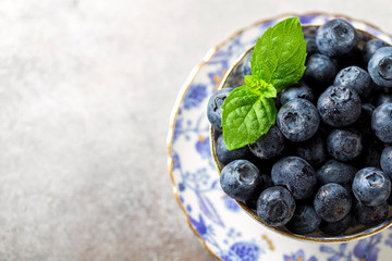 Fresh juicy blueberries in a vintage porcelain cup on a light concrete background. Healthy food or nutrition.