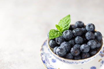 Fresh juicy blueberries in a vintage porcelain cup on a light concrete background. Healthy food or nutrition.