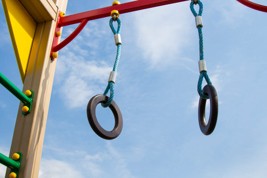 Gymnastics rings hang on the playground on the horizontal bar. Against the blue sky