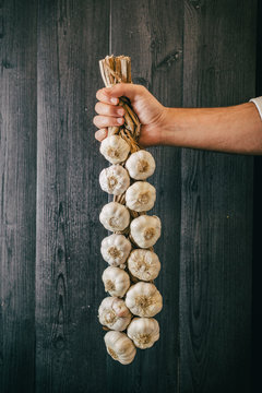 Unrecognizable person holding and showing a bunch of healthy fresh garlic against black lumber wall