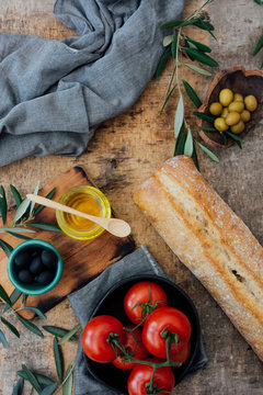 Top view composition of fresh homemade bread loaf placed on wooden table near ripe red tomatoes with green and black olives and olive oil