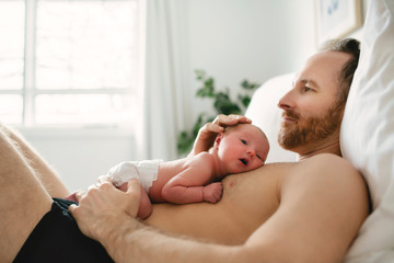 A father with a newborn baby in bed