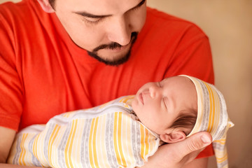 Happy dad rocking in arms sleeping infant child in striped cap. Close up portrait of father holding cute newborn baby daughter and looking with love. Fathers day and man on parental leave concept