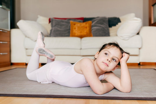 Bored thoughtful little girl in leotard lying on the floor looking away while resting during ballet rehearsal at home