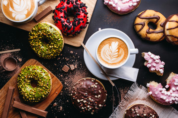 Various doughnuts with sweet toppings and chocolate bars composed with cup of cappuccino on black table