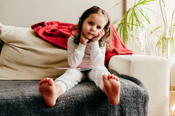 Cute little girl sitting on the couch with a notebook looking for inspiration