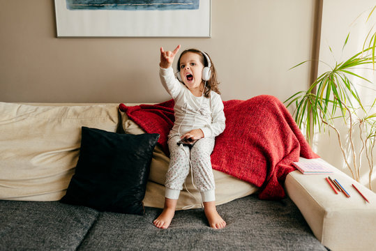Cute little girl sitting on the couch listening music with headphones