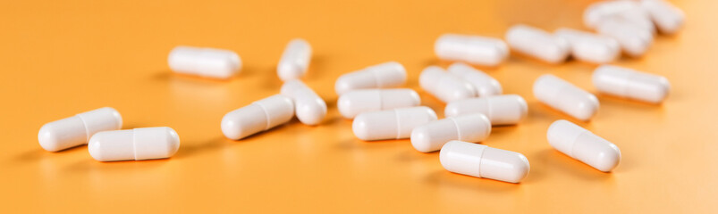Pharmaceutical medicine white pills, tablets or capsules on yellow background.